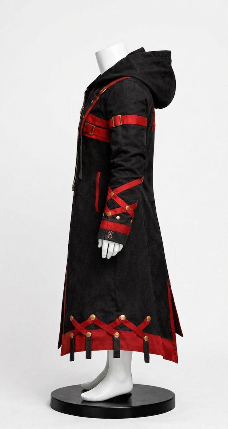 May include: Black hooded coat with red accents. The long coat features red straps, gold-colored buttons, and decorative red trim. The sleeves have a crisscross design with gold buttons. The coat is displayed on a mannequin.