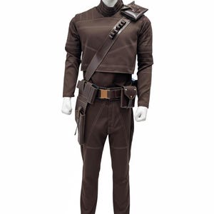 May include: Brown costume with white stitching, displayed on a mannequin. The outfit includes a long-sleeved top, pants, belt with a gold buckle, and multiple pouches. A strap with pouches goes across the chest.