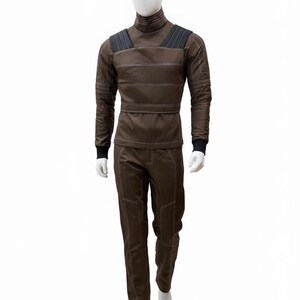 May include: A brown jumpsuit with white stitching and black accents on a mannequin. The long-sleeved top has a high collar and shoulder pads. The pants have reinforced knee patches. The mannequin is on a white background.