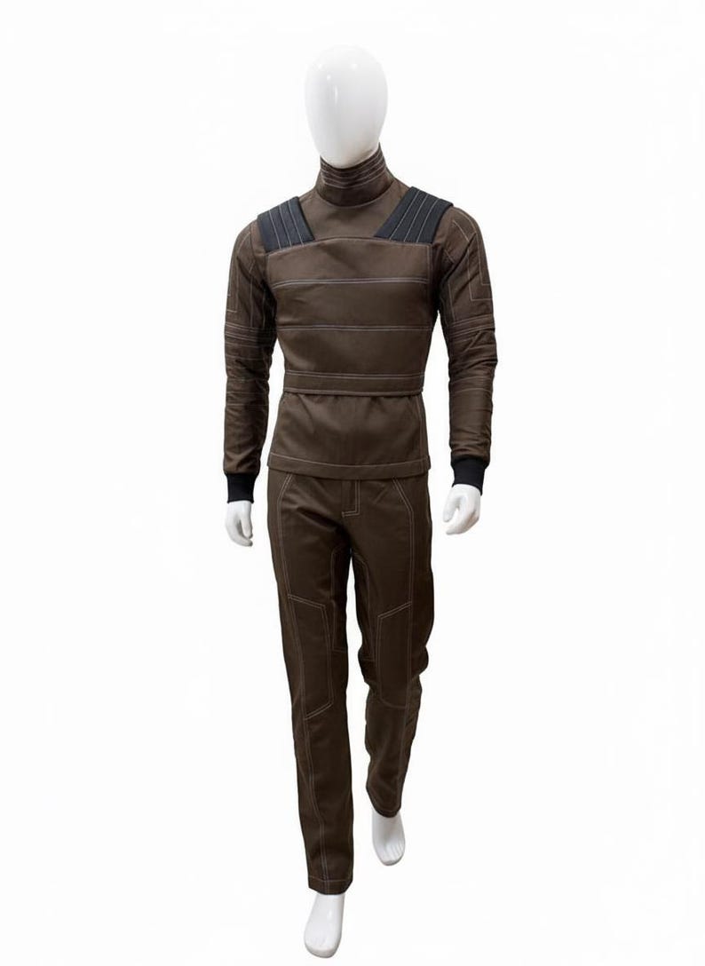 May include: A brown jumpsuit with white stitching and black accents on a mannequin. The long-sleeved top has a high collar and shoulder pads. The pants have reinforced knee patches. The mannequin is on a white background.