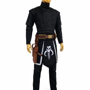 May include: Black costume with a high collar, brown belt with ammunition and a holster. The costume includes a black apron with a white skull design. The outfit is displayed on a mannequin.