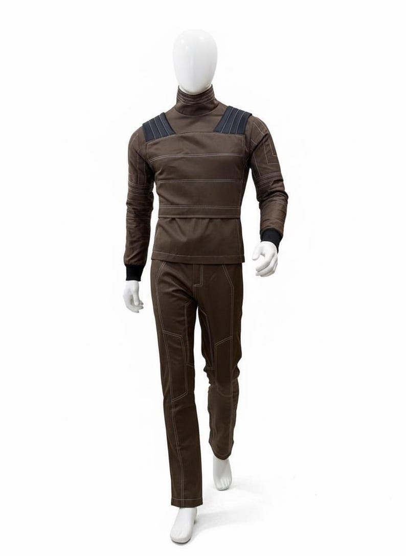 May include: A brown jumpsuit displayed on a mannequin. The outfit features a high collar, long sleeves, and pants. White stitching outlines the seams and panels. Black accents are on the shoulders and wrists. The mannequin is white, and the background is plain.