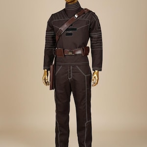 Puede incluir: Un uniforme marr&oacute;n con costuras blancas, exhibido en un maniqu&iacute;. El atuendo incluye una parte superior de manga larga, pantalones y un cintur&oacute;n con funda. Una correa de hombro marr&oacute;n y un cuello alto completan el look.