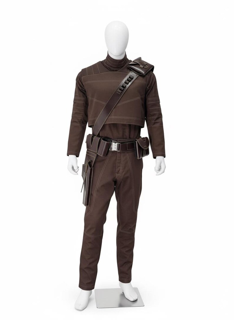 May include: Brown costume with a high collar, long sleeves, and visible stitching. The outfit includes matching pants, a belt with pouches, and a shoulder strap with a rectangular accent. The mannequin is on a silver base.