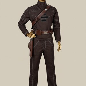 Puede incluir: Un disfraz marr&oacute;n con costuras blancas, exhibido en un maniqu&iacute;. El atuendo incluye una parte superior de manga larga, pantalones y un cintur&oacute;n con una funda. Una correa de hombro marr&oacute;n y un cuello alto completan el look. El disfraz es probablemente para cosplay o un evento tem&aacute;tico.