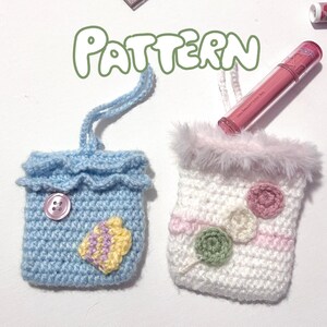 Może przedstawiać: Dwie ręcznie robione szydełkowe saszetki. Jedna jest jasnoniebieska z falbanką na górze, guzikiem i żółto-fioletową aplikacją. Druga jest biała z różowymi i zielonymi kwiatowymi akcentami i puszystym różowym wykończeniem. Słowo "PATTERN" jest napisane na zielono.