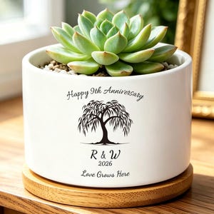 May include: A white ceramic plant pot with a succulent, on a wooden base. The pot is inscribed with "Happy 9th Anniversary", a tree illustration, and the text "R & W 2026 Love Grows Here".