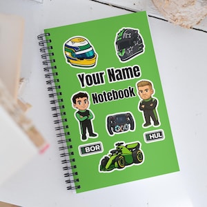 May include: A green spiral-bound notebook with the text "Your Name Notebook". The notebook is decorated with stickers of racing helmets, race car drivers, a steering wheel, and a green race car.