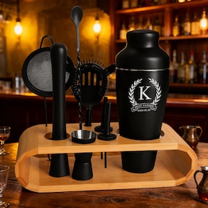 Pode incluir: Um conjunto de bar preto com base de madeira. O conjunto inclui um shaker, coador, pilão, colher de bar e jigger. O shaker tem um "K" branco e o texto "BEST FATHER 2025.02.28".