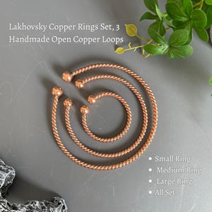 Może przedstawiać: Zestaw trzech ręcznie wykonanych otwartych miedzianych pierścieni, określonych jako Lakhovsky Copper Rings Set. Pierścienie mają skręconą metalową fakturę z zaokrąglonymi końcami. Tekst na obrazku brzmi: Lakhovsky Copper Rings Set, 3 Handmade Open Copper Loops, Small Ring, Medium Ring, Large Ring, All Set.