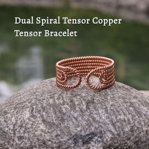 May include: A copper tensor bracelet with a dual spiral design. The bracelet is made of coiled copper wire and features the text "Dual Spiral Tensor Copper Tensor Bracelet". The bracelet is displayed on a gray stone.