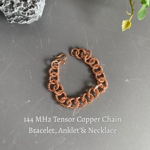 May include: A copper chain bracelet featuring twisted metal links and a hook clasp. The text 144 MHz Tensor Copper Chain Bracelet, Anklet & Necklace is printed below the jewelry. The chain is constructed from individual circular copper segments.