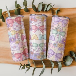 Può includere: Tre bicchieri isolati dai colori pastello con disegni floreali e fiocchi. La parola "MAMA" è visualizzata sul bicchiere centrale. I bicchieri hanno una combinazione di colori rosa chiaro, giallo e viola con un motivo a scacchi.