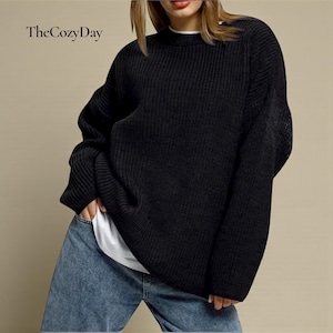 May include: Black crew neck knit sweater with long sleeves. The Cozy Day text is in the upper left corner. The sweater is worn with blue jeans and a white t-shirt.