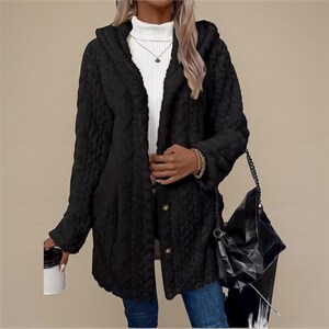 Peut inclure: Un manteau noir à capuche avec un aspect pelucheux texturé. Le manteau a une fermeture boutonnée sur le devant et une coupe décontractée. Un sac à main noir avec une bandoulière en chaîne est suspendu à l'épaule.