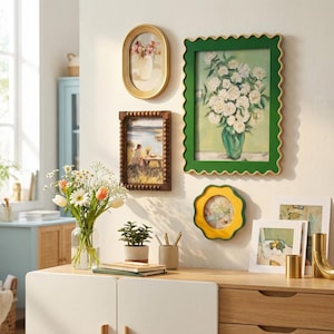 May include: A gallery wall arrangement featuring an oval gold frame, a rectangular dark wood beaded frame, a large rectangular green scalloped frame with a floral print, and a small yellow scalloped frame, all displayed on a light wall.