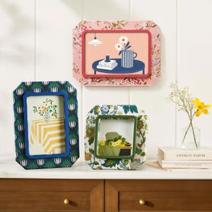 May include: Three decorative picture frames with floral patterns. One frame has a pink floral design, another has a blue and green floral design, and the third has a green and white floral design. Each frame holds a different illustration.