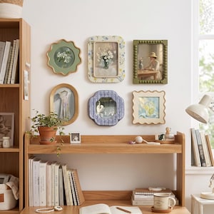 May include: A collection of six decorative wall frames featuring diverse shapes and colors, including scalloped, beaded, and floral patterns, displaying various artistic prints of flowers, a person, a dress, a swan, and a glass of lemonade.