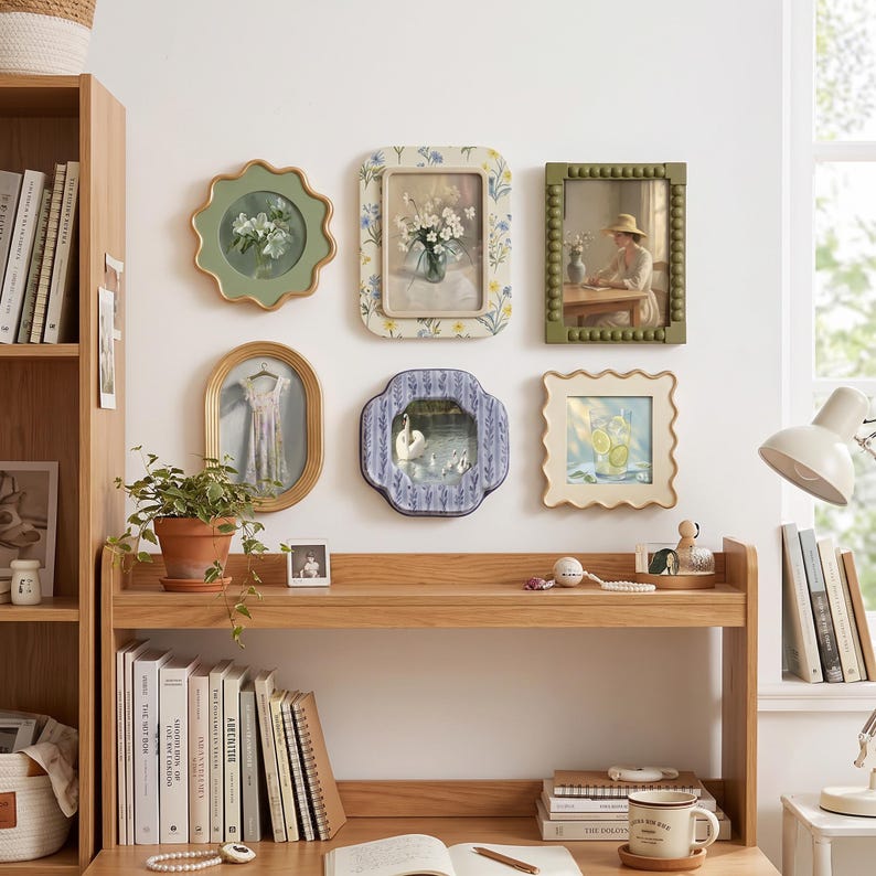 May include: A collection of six decorative wall frames featuring diverse shapes and colors, including scalloped, beaded, and floral patterns, displaying various artistic prints of flowers, a person, a dress, a swan, and a glass of lemonade.