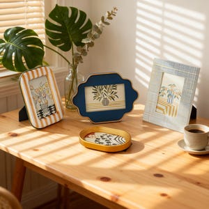 Peut inclure: Plusieurs cadres photo décoratifs de différentes formes et tailles, dont un cadre rayé, un cadre bleu festonné et un cadre bleu texturé. Chaque cadre contient une impression florale. Un petit plateau ovale et une tasse de café sont également sur la table en bois.