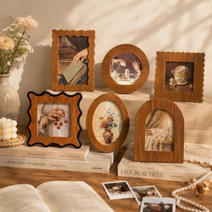 May include: A collection of six wooden picture frames in various shapes including rectangular, square, oval, and arched. The frames feature natural wood grain textures and scalloped edges on some pieces, displaying diverse art prints of still life scenes.