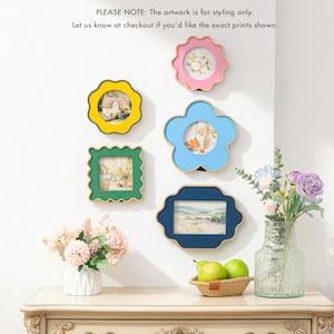 May include: A collection of colorful picture frames in various shapes, including a flower, a scalloped circle, and a square. The frames are in shades of yellow, pink, blue, green, and navy. The text in the image says, "PLEASE NOTE: The artwork is for styling only."