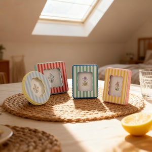 May include: Four colorful picture frames with striped patterns in red, blue, green, and yellow. Each frame has a scalloped edge and a floral design inside. The frames are arranged on a woven mat.