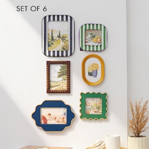 Puede incluir: Conjunto de 6 marcos de fotos decorativos de varias formas y colores. Incluye un marco a rayas, un marco marrón, un marco azul, un marco verde y dos marcos dorados. Cada marco contiene una imagen diferente, incluyendo paisajes y naturalezas muertas.