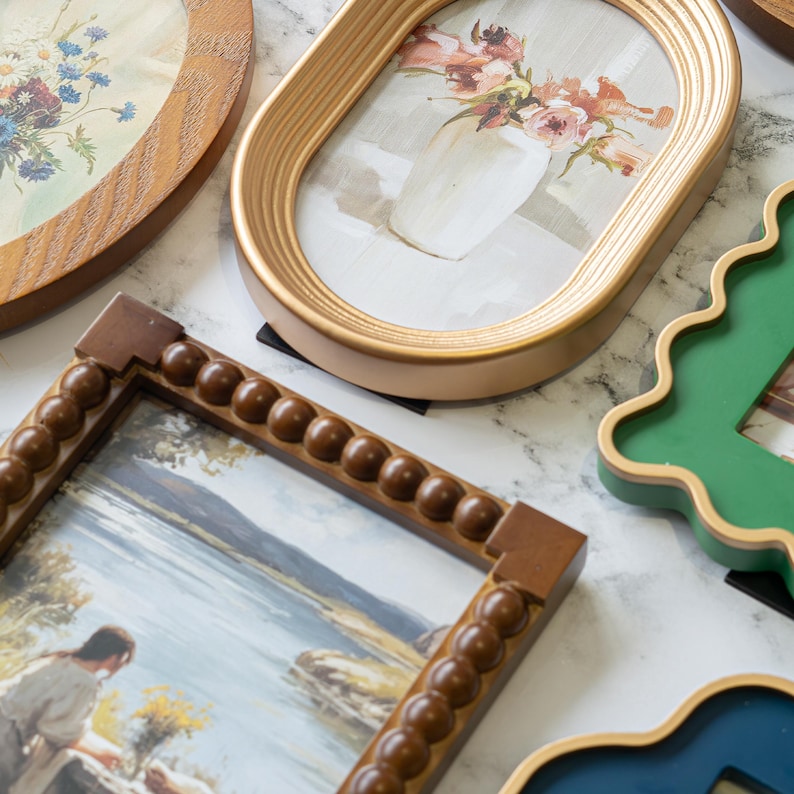 May include: A collection of decorative picture frames in various shapes and colors. The frames include oval, rectangular, and uniquely shaped designs. The frames are made of wood and have different finishes, including gold, brown, and green.