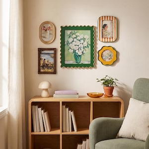 May include: A gallery wall arrangement featuring five diverse picture frames, including a large scalloped green frame with a floral painting, surrounding a wooden bookshelf with books, a mushroom lamp, and a small potted plant.