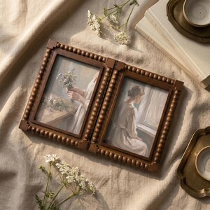 May include: A double-hinged wooden picture frame with a beaded border design. The left frame displays an illustration of hands holding a bouquet of flowers, while the right frame shows an illustration of a person in a light-colored dress near a window.