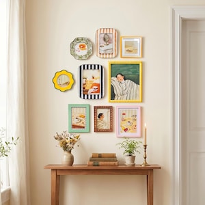 May include: A collection of framed art pieces in various shapes and sizes, including a yellow scalloped mirror and a green gingham-framed picture. The frames are in shades of yellow, pink, green, and brown, creating a gallery wall aesthetic.