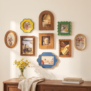 Puede incluir: Una composición de pared de galería con ocho marcos de fotos de diversas formas, incluyendo diseños ovalados, arqueados, festoneados y rectangulares, en tonos madera, amarillo, verde y azul, con láminas de bodegones.