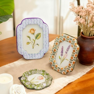 Può includere: Tre cornici decorative con disegni floreali. Una cornice ha un motivo a righe lavanda e bianco con un'illustrazione di rosa gialla. Un'altra presenta un bordo floreale arancione e giallo con un rametto di lavanda. Una terza cornice ha un bordo floreale verde con un tulipano.