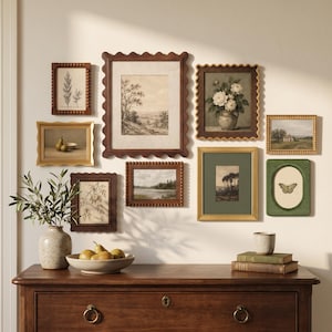 May include: A gallery wall arrangement featuring eight assorted rectangular and oval frames in wood, gold, and green finishes, displaying botanical, landscape, and still life prints, positioned above a wooden dresser with two drawers.