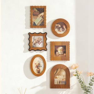 May include: A selection of wooden picture frames in diverse shapes, such as oval, round, square, and arched. Each frame displays a vintage-style image, forming a gallery wall arrangement. The frames are a warm brown hue and are mounted on a white wall.