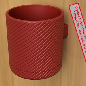 Może przedstawiać: Cylindryczny, czerwony pojemnik z teksturowanym, ukośnym wzorem w paski. Mały uchwyt jest przymocowany z boku. Widoczna jest etykieta z niemieckim tekstem. Etykieta mówi "Digital file - not a physical item!"