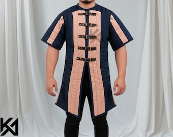 May include: A navy blue and peach-colored padded gambeson with short sleeves. The front features vertical peach panels and leather straps with buckles. The garment is designed for historical reenactment or costume use.