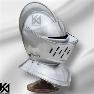 Könnte beinhalten: Ein polierter silberner Ritterhelm mit Visier und Nackenschutz, montiert auf einem Holzständer. Der Helm hat Belüftungslöcher und den Text "KNIGHTS ARMOURY".