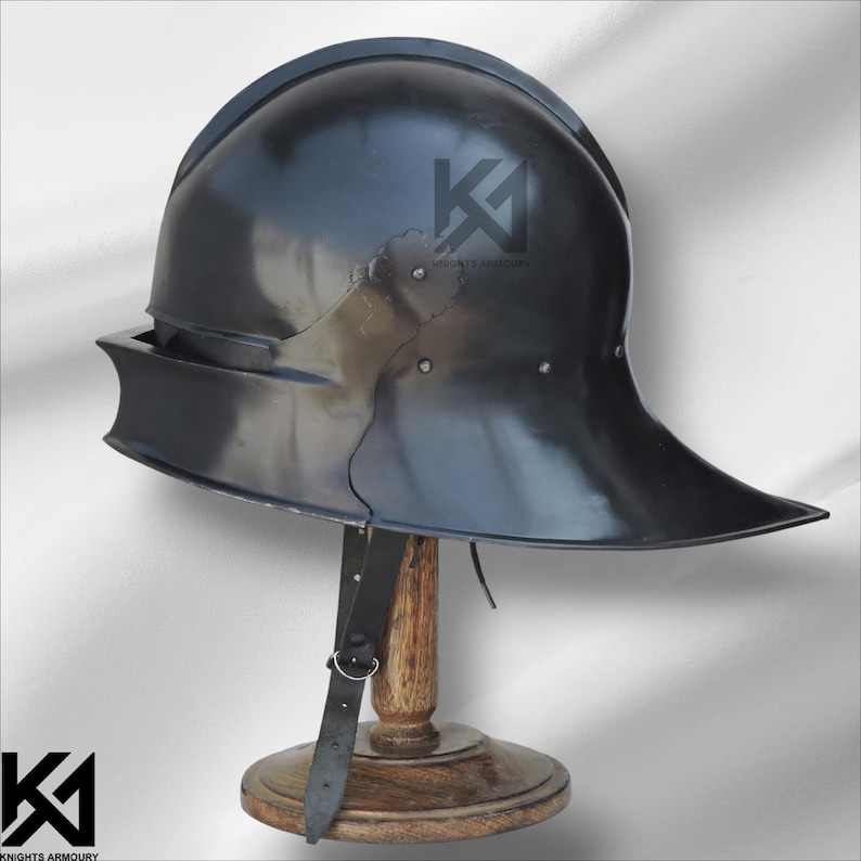 Op de afbeelding: Een zwarte metalen helm met een brede rand en een afgeronde bovenkant, tentoongesteld op een houten standaard. De helm heeft een glanzende afwerking en een leren riem. Het logo "KNIGHTS ARMOURY" is zichtbaar.