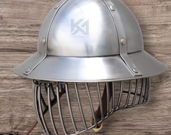 May include: A silver-colored helmet with a rounded top and a wide brim. The helmet features a cage-like face guard and is secured with rivets and straps. The text "KNIGHTS ARMOURY" is visible on the helmet.
