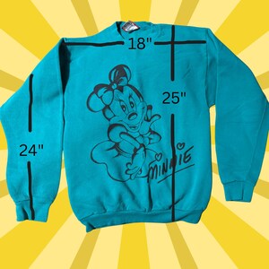 May include: Teal sweatshirt featuring a black graphic of Minnie Mouse with a bow. The sweatshirt measures 18 inches across the chest, 25 inches in length, and 24 inches for the sleeve length. The word "Minnie" is written in a cursive font.