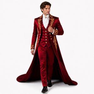 Op de afbeelding: Een formeel rood fluwelen pak met gouden borduursels. Het pak bestaat uit een lange jas, een vest en een broek. De jas heeft sierlijke gouden details op de mouwen en revers. Het vest heeft gouden knopen. Een wit gerimpeld overhemd maakt de outfit compleet.