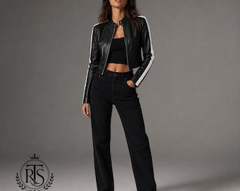 Op de afbeelding: Een zwart kort leren jasje met witte strepen langs de mouwen, gedragen over een zwarte crop top en gecombineerd met een zwarte spijkerbroek met hoge taille. De outfit wordt gecompleteerd met zwarte laarzen met een puntige neus voor een look.