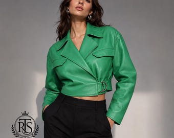 May include: A cropped bright green jacket with a wide collar, long sleeves, and two chest pockets. The jacket features a wrap-style front closure secured with a silver-toned metal buckle and strap detail at the waist, paired with black trousers.