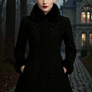 May include: A long black coat with a faux fur collar and cuffs. The coat features intricate embroidered detailing down the front and is buttoned up. The person is standing on a cobblestone path in front of a large house.