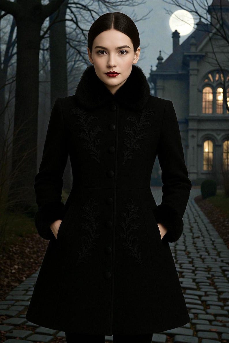 May include: A long black coat with a faux fur collar and cuffs. The coat features intricate embroidered detailing down the front and is buttoned up. The person is standing on a cobblestone path in front of a large house.