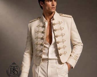 May include: An off-white military-style jacket featuring gold-toned braided cord detailing, decorative gold buttons, and structured epaulets on the shoulders. The jacket is worn open over a matching off-white shirt and trousers, creating a uniform look.