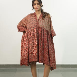 Könnte beinhalten: Ein knielanges Kleid mit einem Patchwork-Design aus verschiedenen floralen und geometrischen Mustern in Rot-, Braun- und Beigetönen. Das Kleidungsstück hat einen V-Ausschnitt, eine durchgehende Knopfleiste und lockere, weite Ärmel.