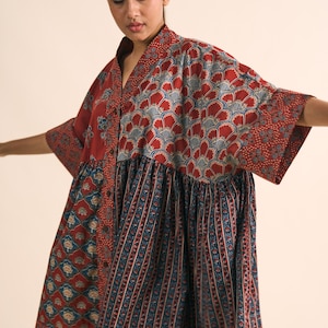 Könnte beinhalten: Gemustertes, rot-blaues Kleid mit kurzen Ärmeln. Das Kleid hat einen V-Ausschnitt und eine Knopfleiste vorne. Der obere Teil hat ein Blumenmuster, während der untere Teil vertikale Streifen hat. Das Kleid ist aus leichtem Stoff.